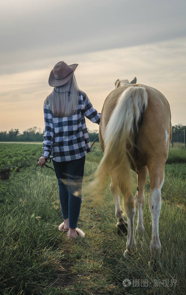 一个年轻的金发女孩戴着帽子穿着格子衬衫晚上牵着一