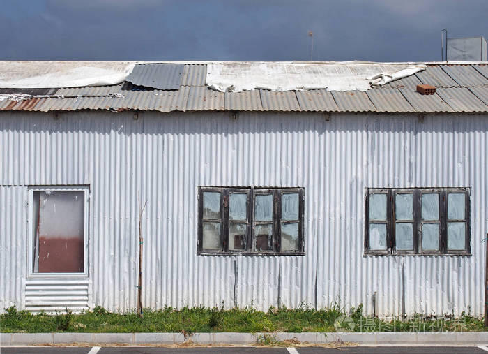 一座破旧破旧的瓦楞铁楼的全画框特写窗户上有封闭的油漆修补了生锈的