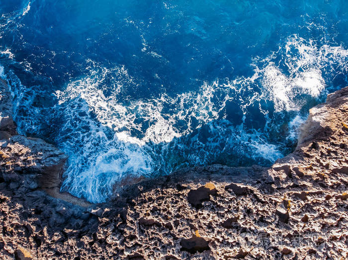 俯视湛蓝的大海,海浪拍打着海滩和岩石.航拍照片.