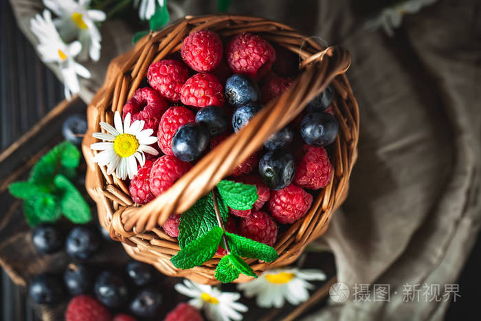 树莓和蓝莓放在黑底洋甘菊和叶子的篮子里夏季健康饮食理念选择性聚焦
