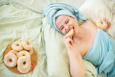头上顶着毛巾的女孩高兴地吃着甜甜圈.照片