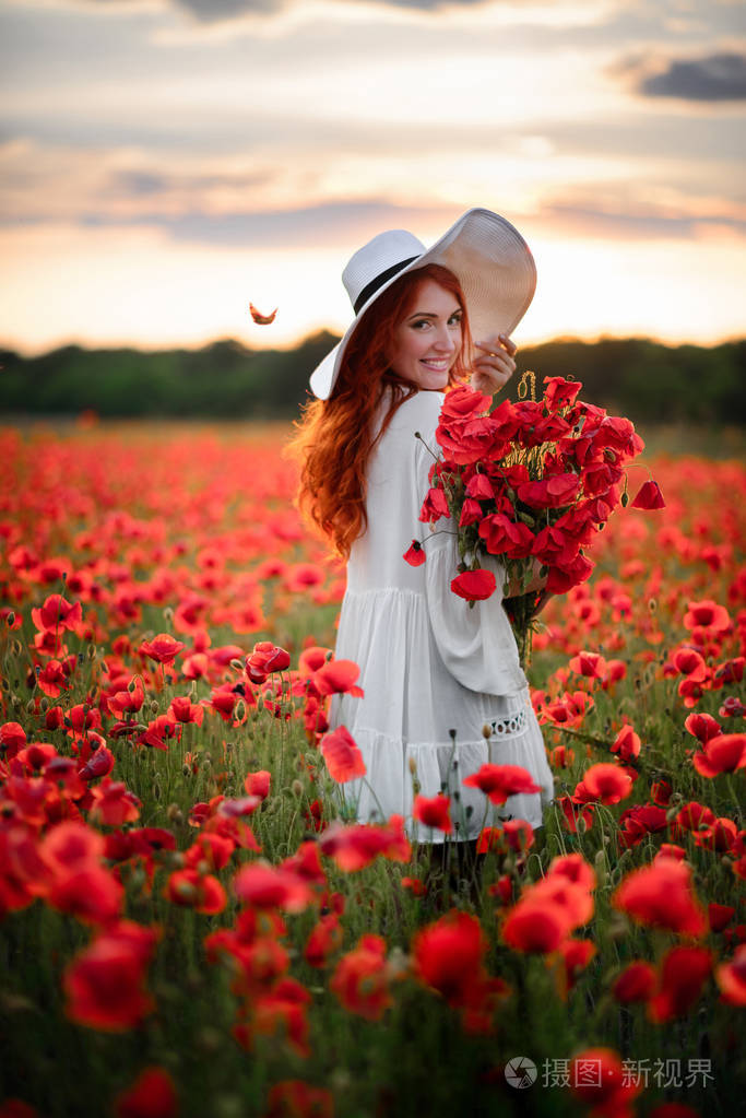 夕阳西下幸福的年轻美丽的女子捧着一束红罂粟花站在花丛中