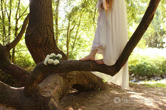 一个穿着白色长裙的女人赤脚在公园的树干上浪漫地散步照片-正版商用