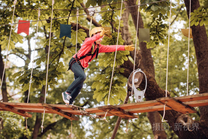 爬树一个漂亮的孩子在树间的绳索公园里的画像头盔儿童玩耍的安全设备