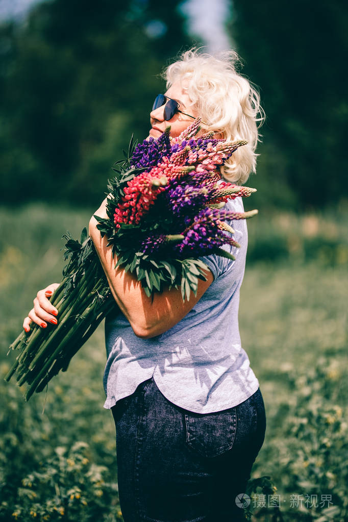 金发,成熟,结实的女人拿着羽扇豆花束在自然背景上.