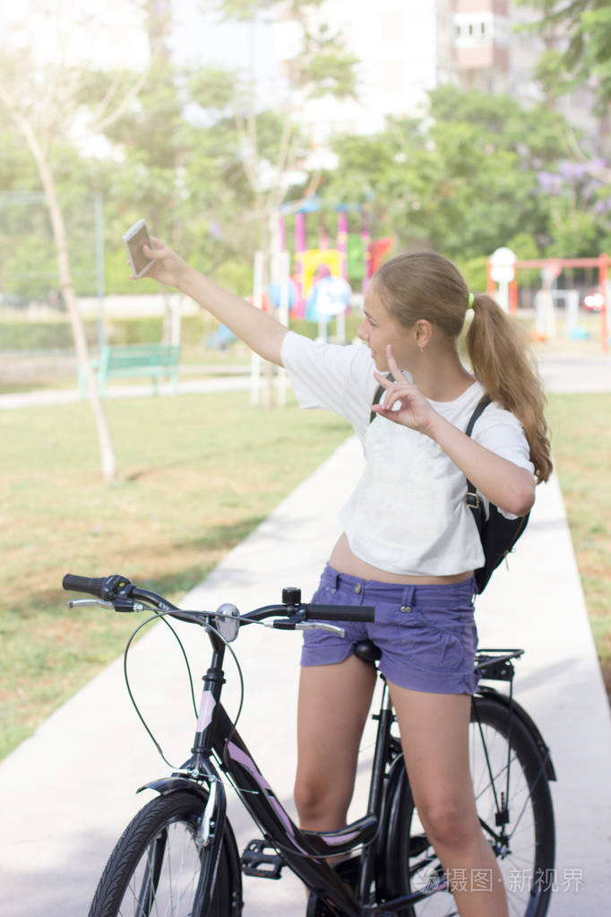 一个时髦的年轻女孩坐在公园里的自行车上自拍
