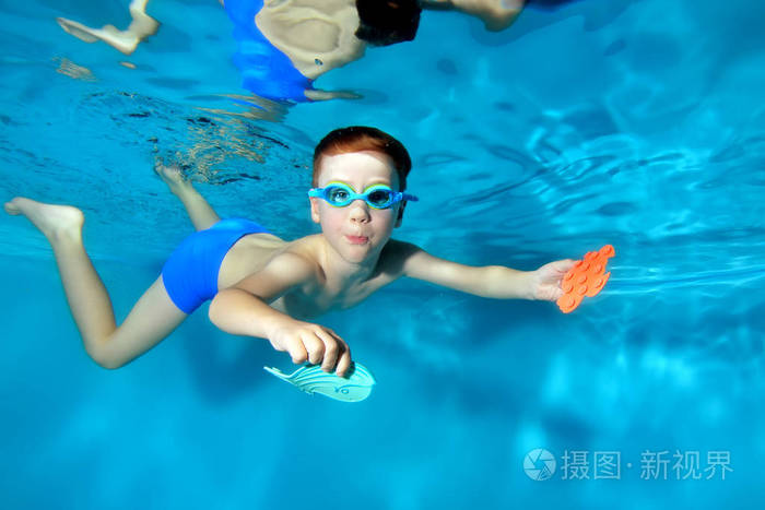 小男孩在水下游泳,带着玩具潜到游泳池的底部.