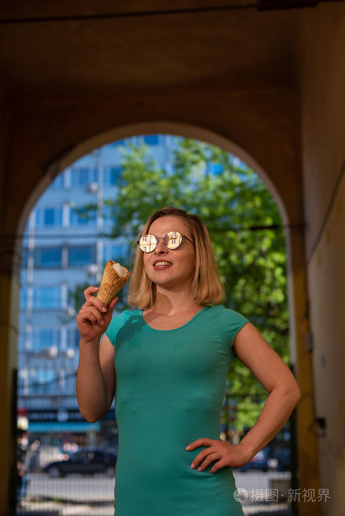 在一个温暖的夏天一个穿着绿松石裙子的快乐女人站在拱形通道里吃华夫