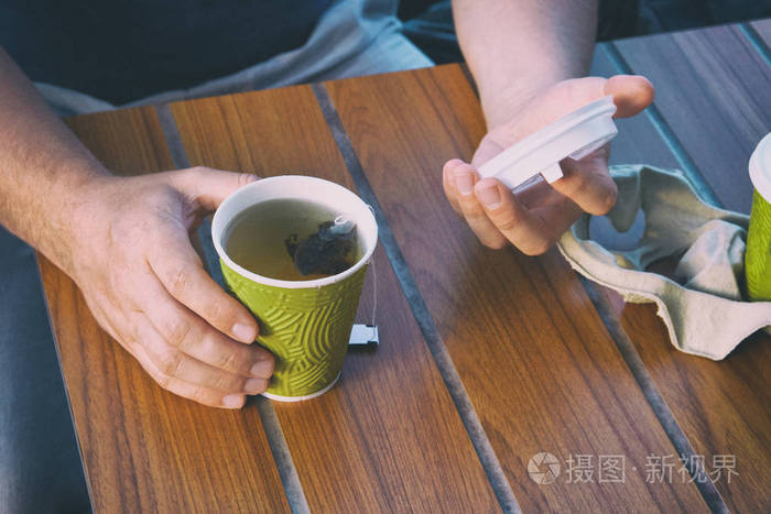 在街边小吃店端着茶杯的男的手木桌上的茶杯色调的图像