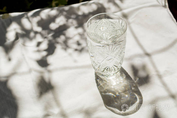 一杯带气泡的清水放在一张白布的桌子上太阳被玻璃和皮影照耀得很美为
