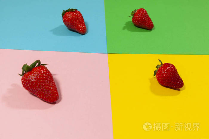 四个完整的草莓放在一个由绿色蓝色粉色和黄色组成的平面上