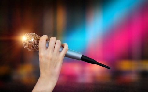 麦克风场景一只女性的手拿着一只麦克风对着卡拉ok俱乐部里五颜六色的