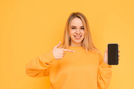 穿着鲜艳衣服的快乐女孩站在黄色背景上,手里拿着一部智能手机,在屏幕