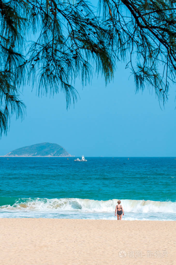 一位身穿黑色紧身泳衣的年轻女子站在沙滩上眺望远方