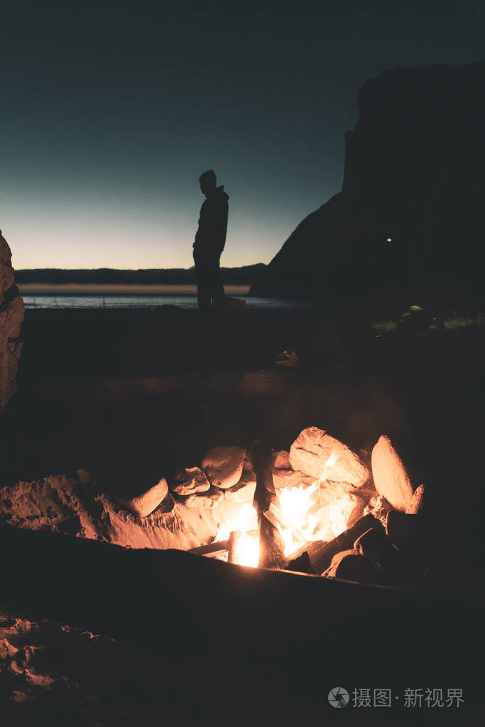 海滩上一个男孩站在篝火后面的剪影