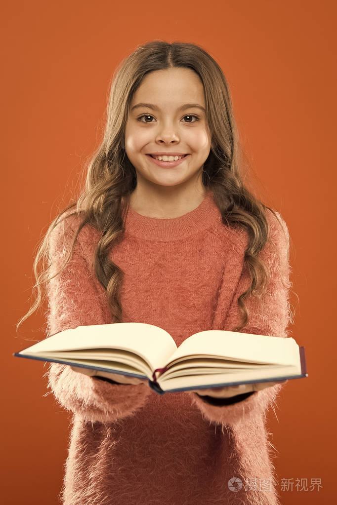 女孩拿着书在橙色背景上读故事.孩子喜欢看书.书店概念.