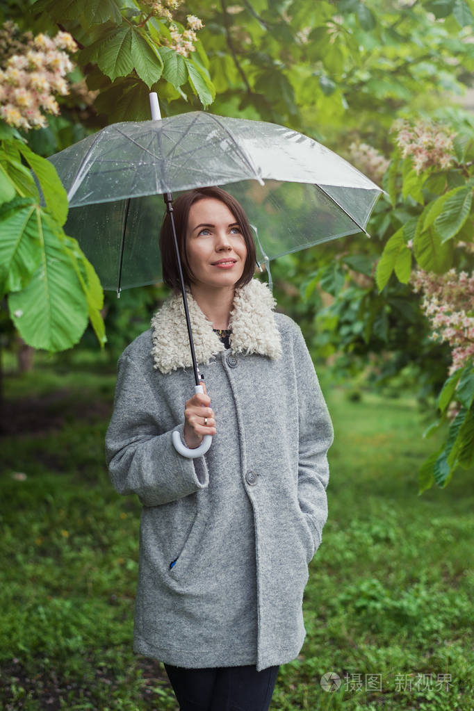 一个穿着外套的女人在雨中撑着伞在绿树下