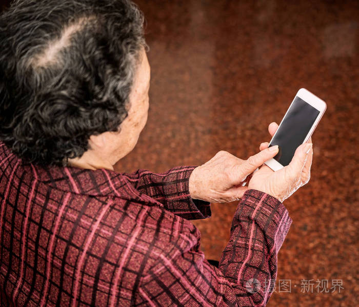 亚洲老年妇女坐在现代智能手机上看东西在家里和别人联系生活科技特写