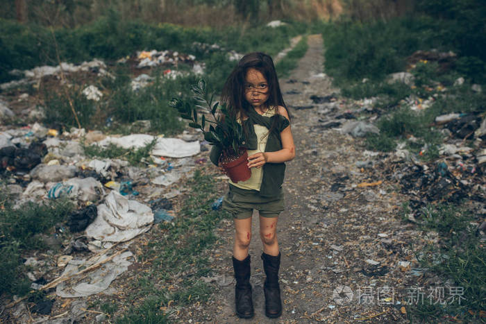 一个无家可归的女孩站在垃圾堆上盆里放着盆栽植物