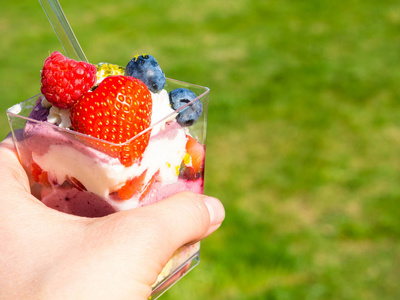 手拿着冰镇甜点奶油和新鲜浆果,健康的夏日甜点照片