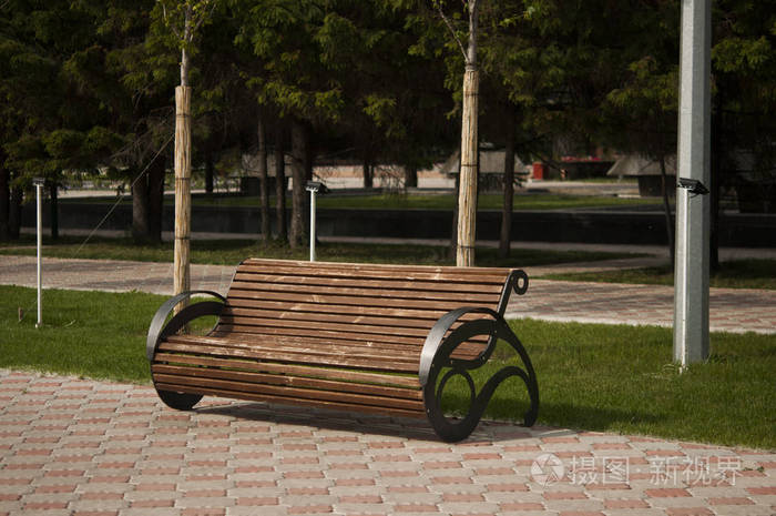 Empty wooden bench in the park beside the grass and path