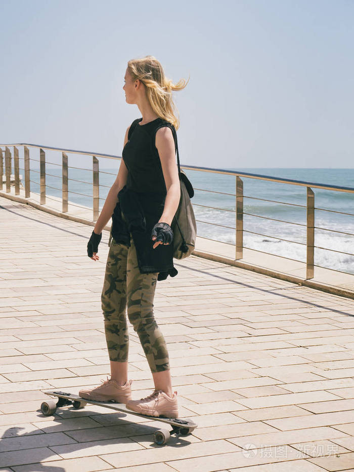 一个美丽的金发女孩在海边的夏日里滑滑板