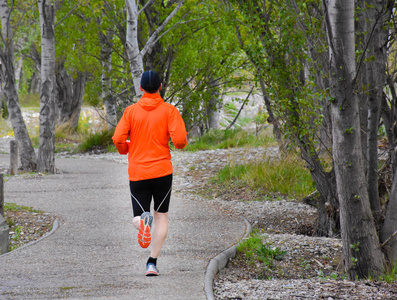 穿着橙色运动衫,黑色短裤和帽子的男子在公园人行道上奔跑的背影.