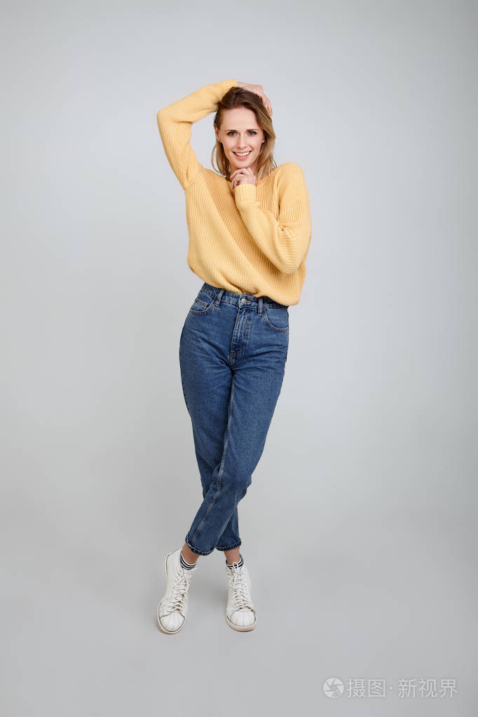 一个穿着时髦衣服的金发美女的全身肖像他一只手握住头发另一只手握住