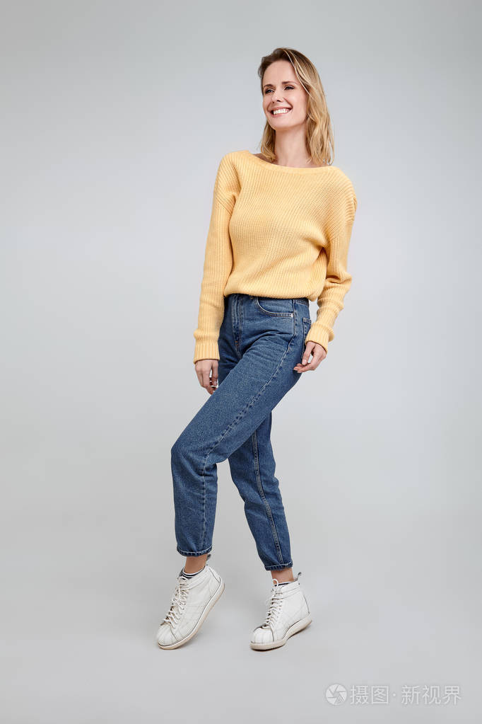 一个穿着时髦衣服的金发美女的全身肖像在白色背景前摆姿势