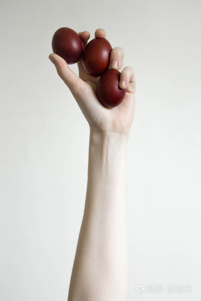 不认识的女人手举着三个鸡蛋敲一个红色的复活节彩蛋古老的节日传统