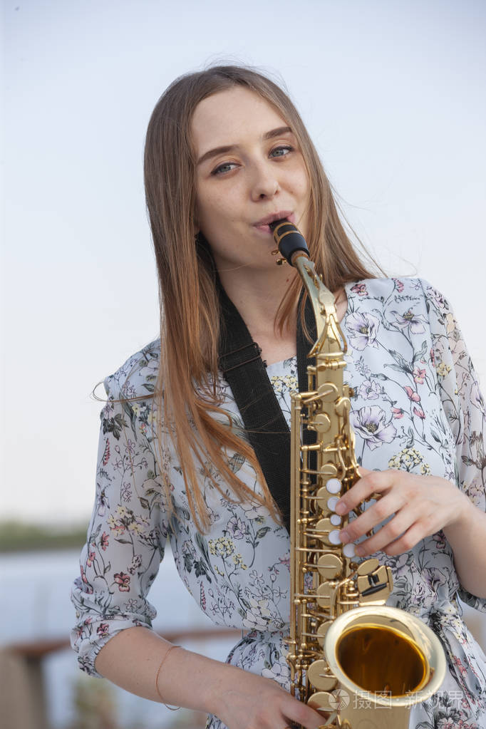 美丽的黑发女子在公园里吹萨克斯管