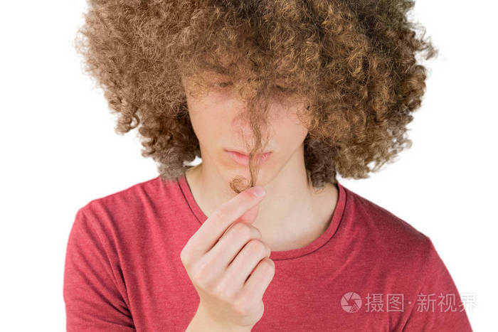 一个年轻的欧洲卷发男人焦急地看着他的长发用手指握着一卷头发很浓密