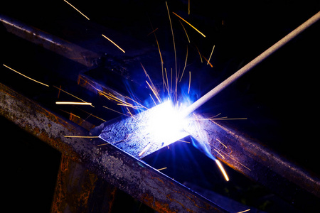 戴防护手套的焊工执行金属结构的电弧焊工艺.电焊机飞溅的火花.