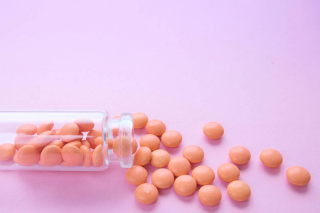 粉红色背景的玻璃瓶上的橙色药片.文本的复制空间.