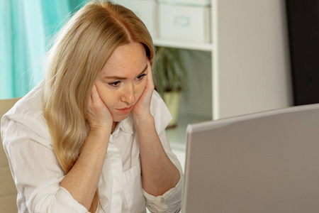 单调乏味无聊的女青年坐在家里的办公桌旁望着远处无法工作的笔记本