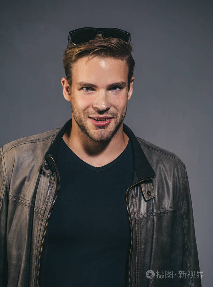 性感帅气时尚男模特表情自信面对镜头穿着皮夹克和墨镜摄影棚在深灰色