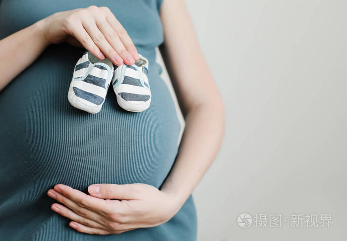 妈妈手拿鞋给新生婴儿孕妇摸肚子快乐的女人怀孕生育身体护理