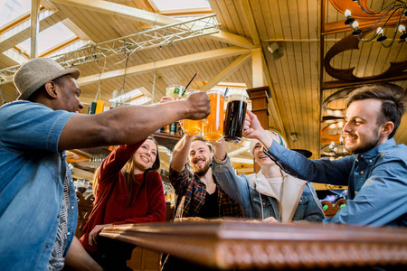 五个朋友喝啤酒和果汁,在咖啡馆吃披萨,各种各样的人在公共场所笑着讲