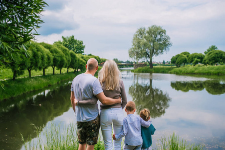 母亲孩子背影两个孩子,妈妈和爸爸看着湖面上夏日的背影.照片