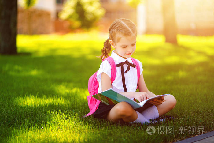 小女生课后背着粉红色的背包坐在草地上看书或学习功课,思考思想,教育