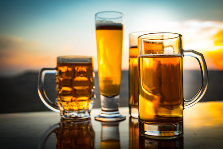 以新鲜的玻璃杯子日落时在海滩上喝一杯啤酒.凉爽的夏季饮料概念.