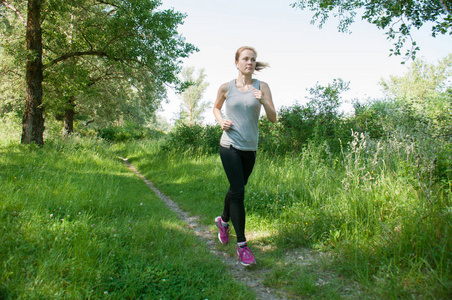 运动,苗条的女人戴着耳机和运动服在公园里奔跑,夏天,阳光明媚的早晨