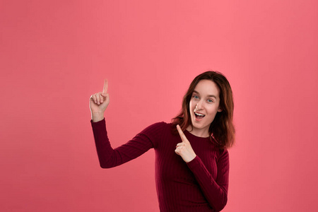 浪漫广告一位快乐的年轻女士,孤独地站在深粉色的背景上,手指着右上角