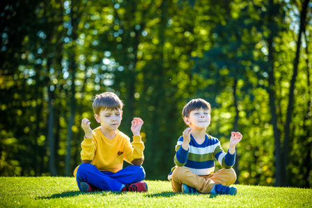 坐在草地垫子上婴儿俯拍两个白人男孩兄弟朋友坐在新鲜的绿色果岭上