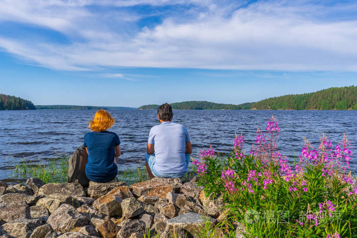 游客们坐在湖湾岸边的石头上,一个黑发男子和一个红头发的年轻女子