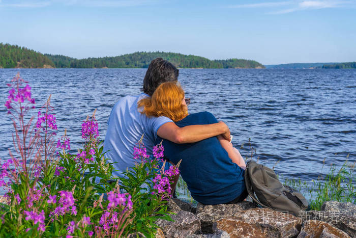 游客们坐在湖湾岸边的石头上,一个黑发男子和一个红头发的年轻女子