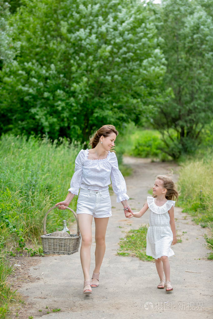 年轻漂亮的妈妈和穿着白裙子的小女儿在野餐时玩得很开心他们手牵着手