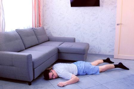 疲惫有趣的书呆子,戴着眼镜和短裤,在家累倒在地上照片