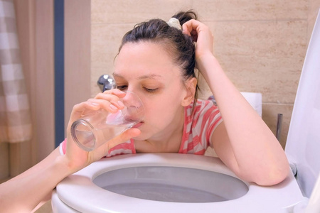生病的妇女坐在家里的地板上,在厕所里呕吐,出现食物中毒症状.照片