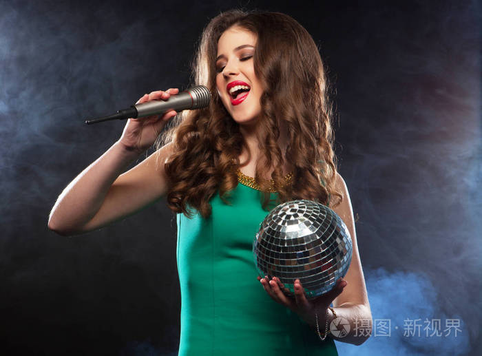 年轻快乐的女孩穿着裙子在聚会上对着麦克风唱歌